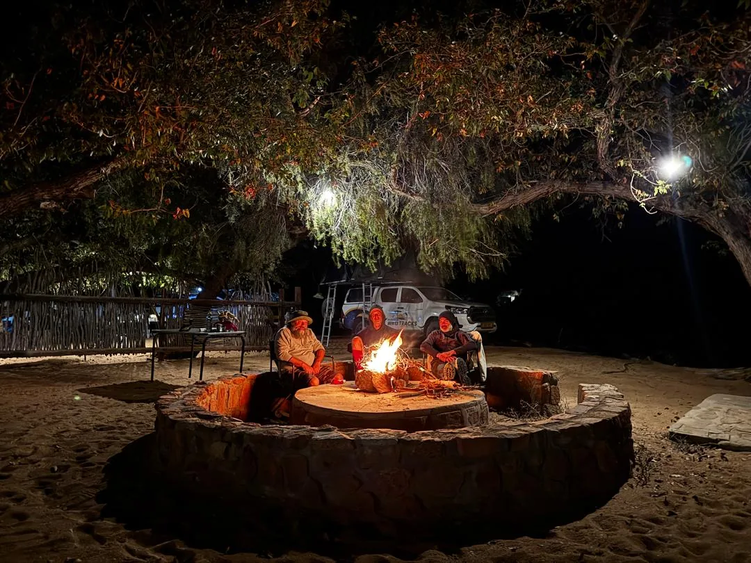 Guests gathered around an Overland Campsite fire at night.