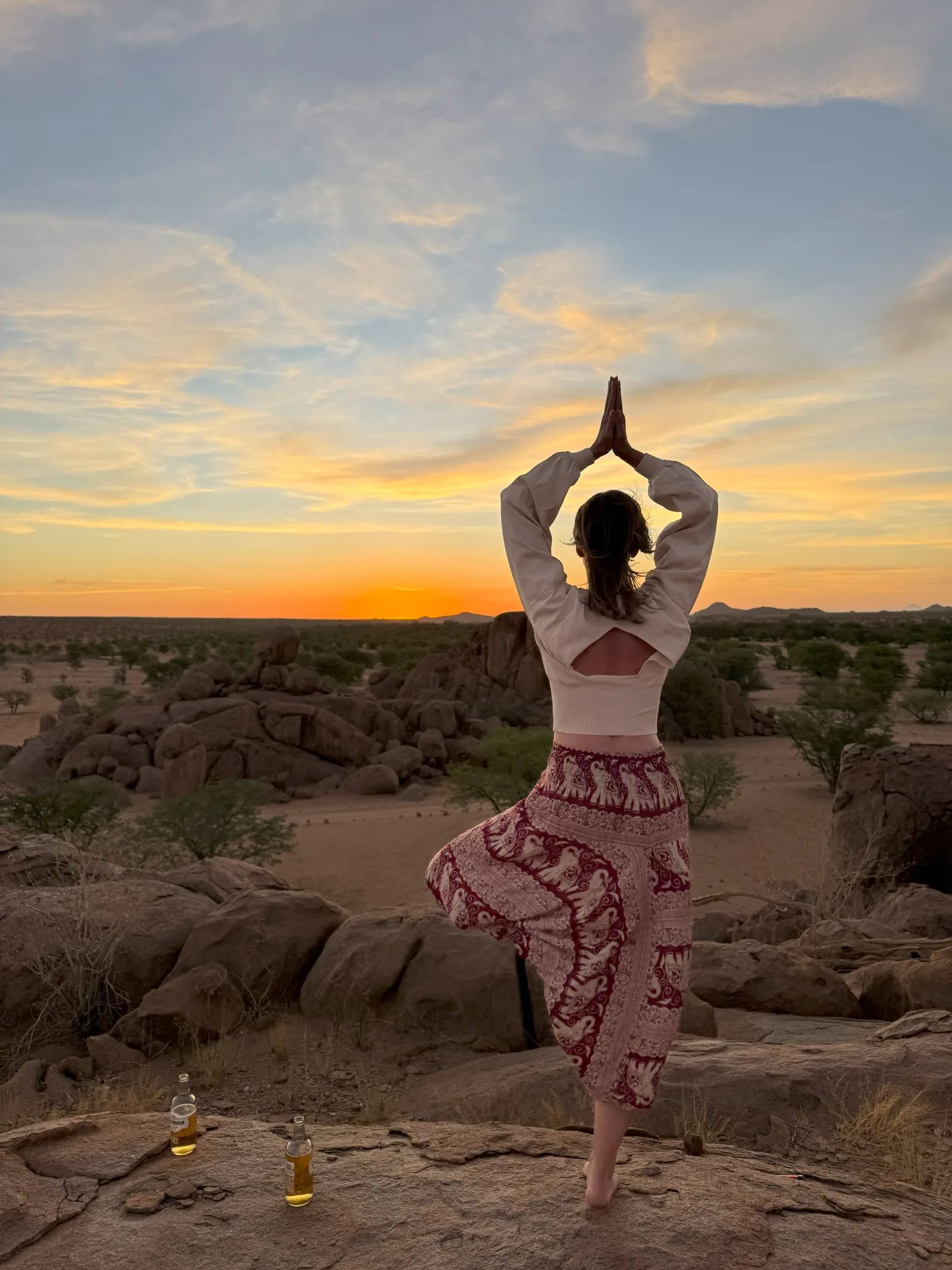 A guest balancing on a granite koppie at sunset with sundowner drinks nearby.