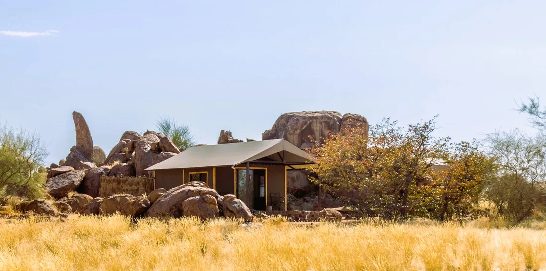 A Madisa safari tent among granite boulders and golden grass.